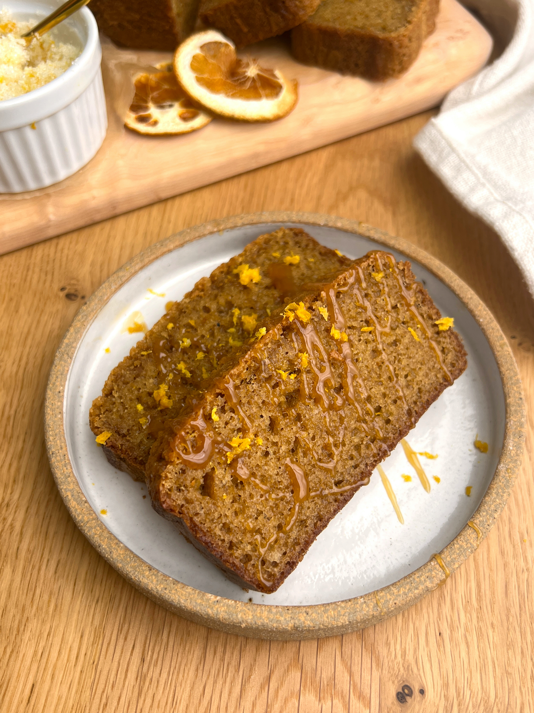 Two Slices of Paleo Almond Orange Loaf on White Plate with Decor in the Background