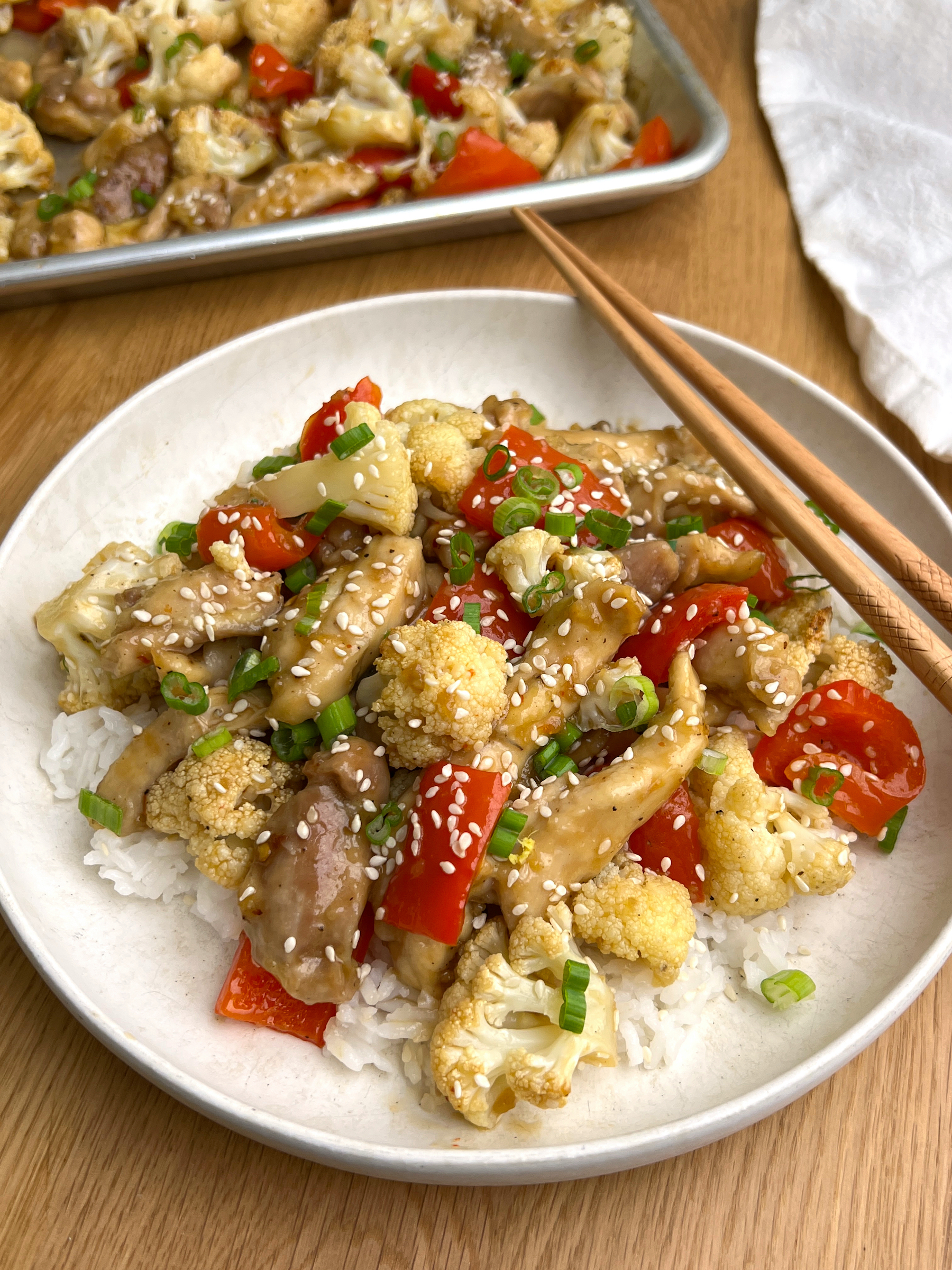 Healthy Kung Pao Chicken & Cauliflower Sheet Pan Meal in white bowl with chopsticks