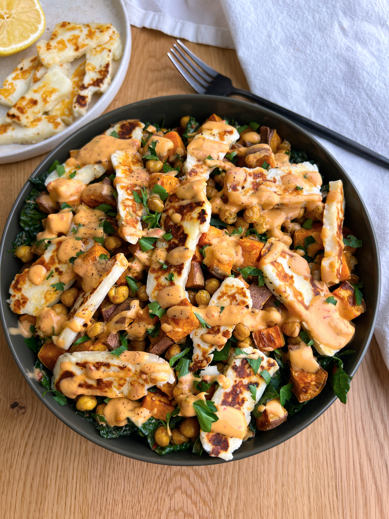 Halloumi and chickpea salad with harissa tahini dressing in green salad bowl