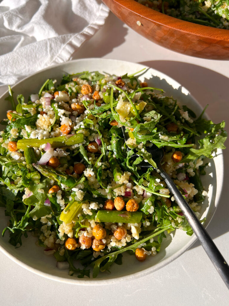 Spring Arugula and Quinoa Salad with Lemon Dressing on white plate with black fork taking a bite out