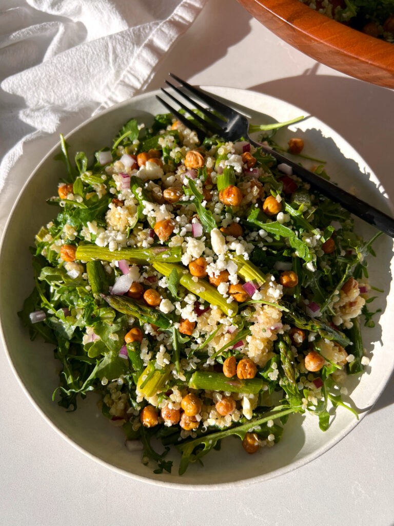 Spring Arugula and Quinoa Salad with Lemon Dressing on white plate with black fork and salad bowl in the background
