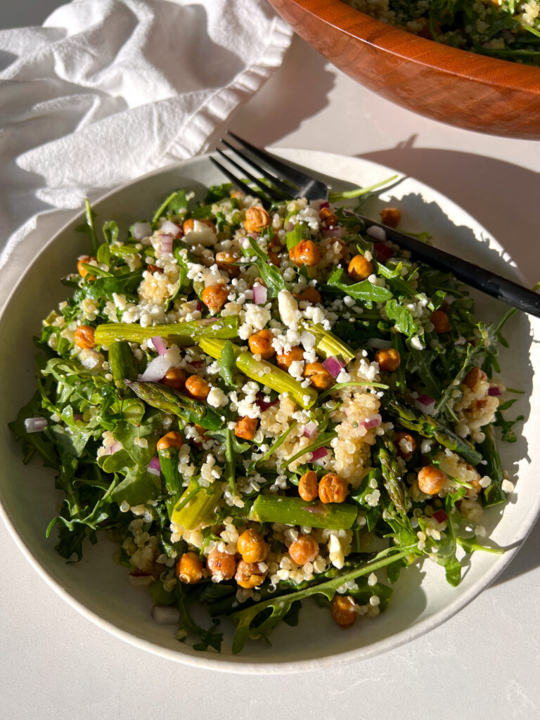 Spring Arugula and Quinoa Salad with Lemon Dressing on white plate with black fork and salad bowl in the background