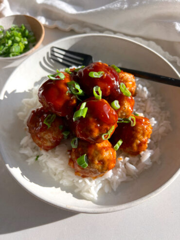 healthy sweet and sour meatballs on white plate with rice, green onion and black fork