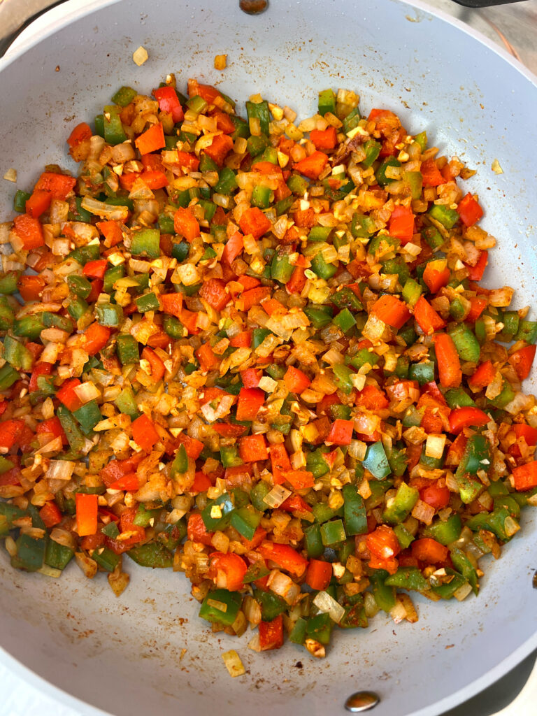 bell peppers, onion, garlic and cajun seasoning cooking in a large pan