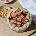 overhead view of high-protein peanut butter and jelly overnight oats in a glass jar topped with strawberries and peanuts
