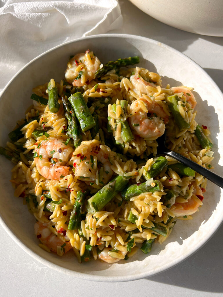 Creamy Shrimp Scampi with Orzo and Asparagus on white plate with black fork taking a bite out