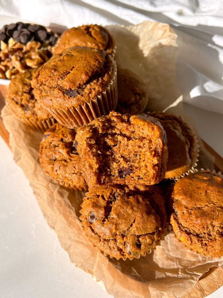 Gluten Free Carrot Cake Muffins with Chocolate Chips stacked on top of each other with a bite taken out of one of them
